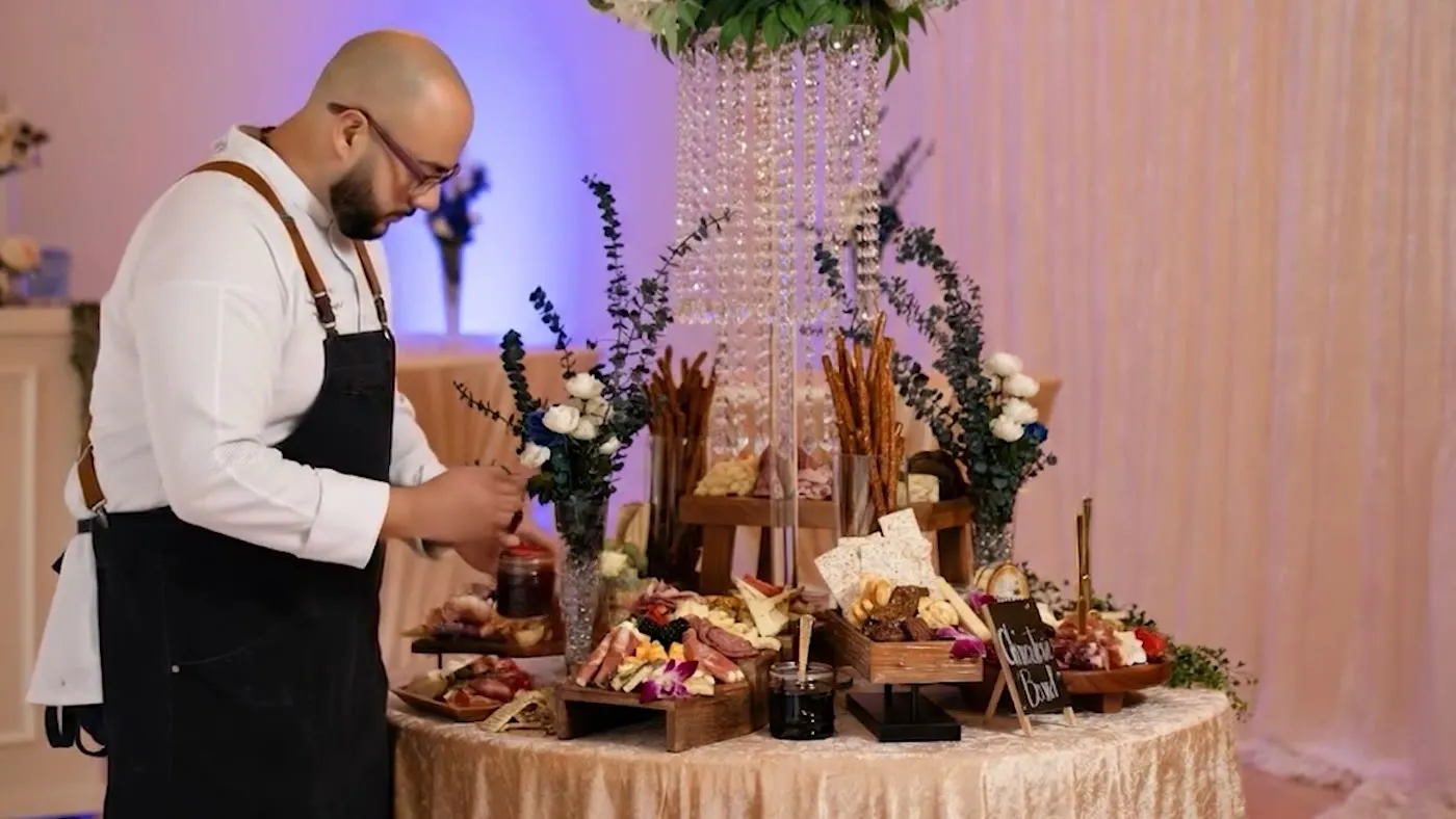 Food station being prepared beside floral decor and a lit ballroom backdrop