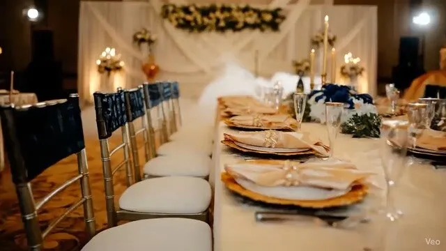 Long decorated guest table with blue chairs, plated settings, and chandelier lighting from the Venue shared album