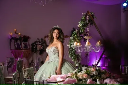 Quinceañera portrait in a green dress beside floral decor and purple uplighting at Nencini Ballroom