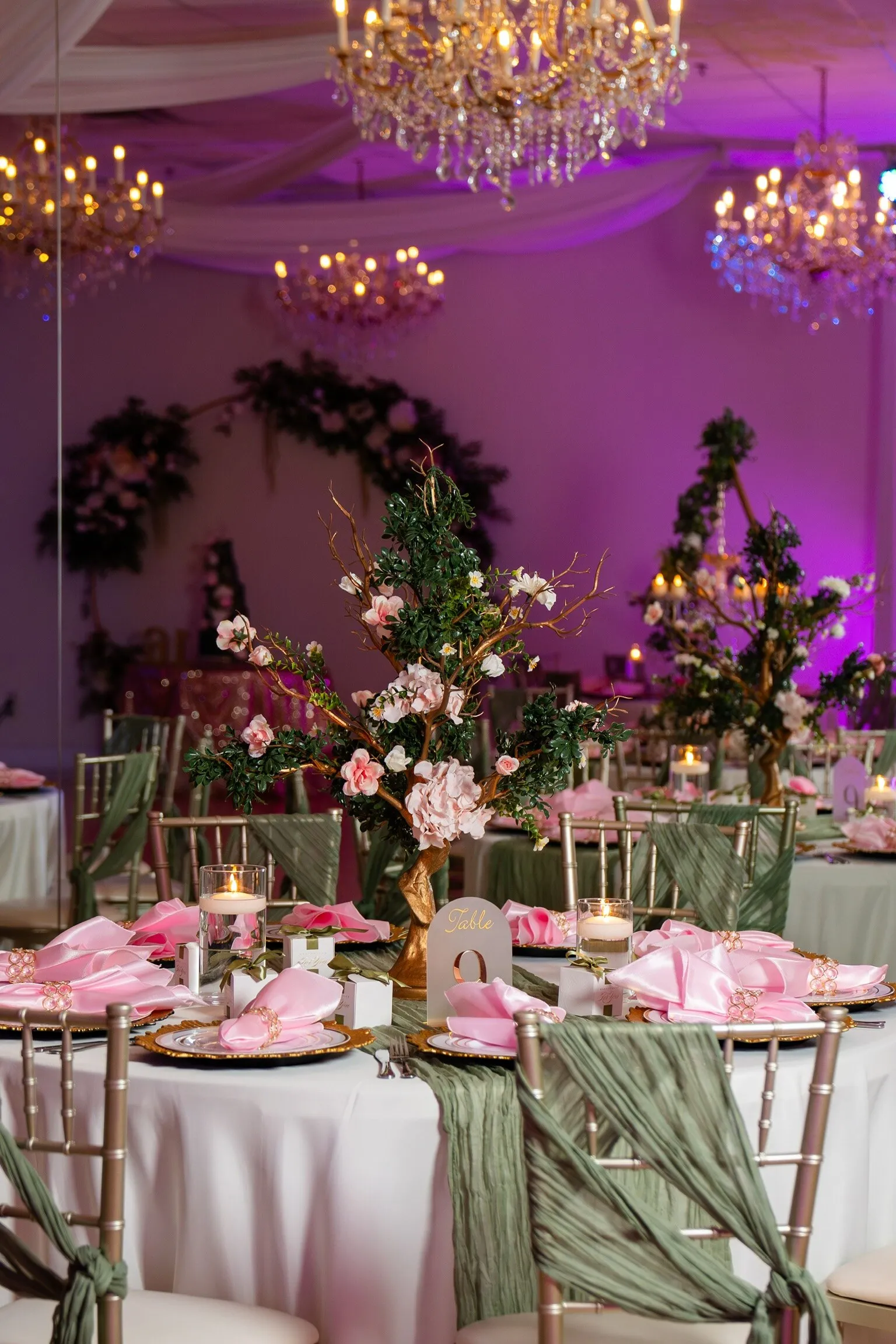 Pink and sage quinceañera table design with chandelier lighting, florals, gold chargers, and candlelight inside Nencini Ballroom