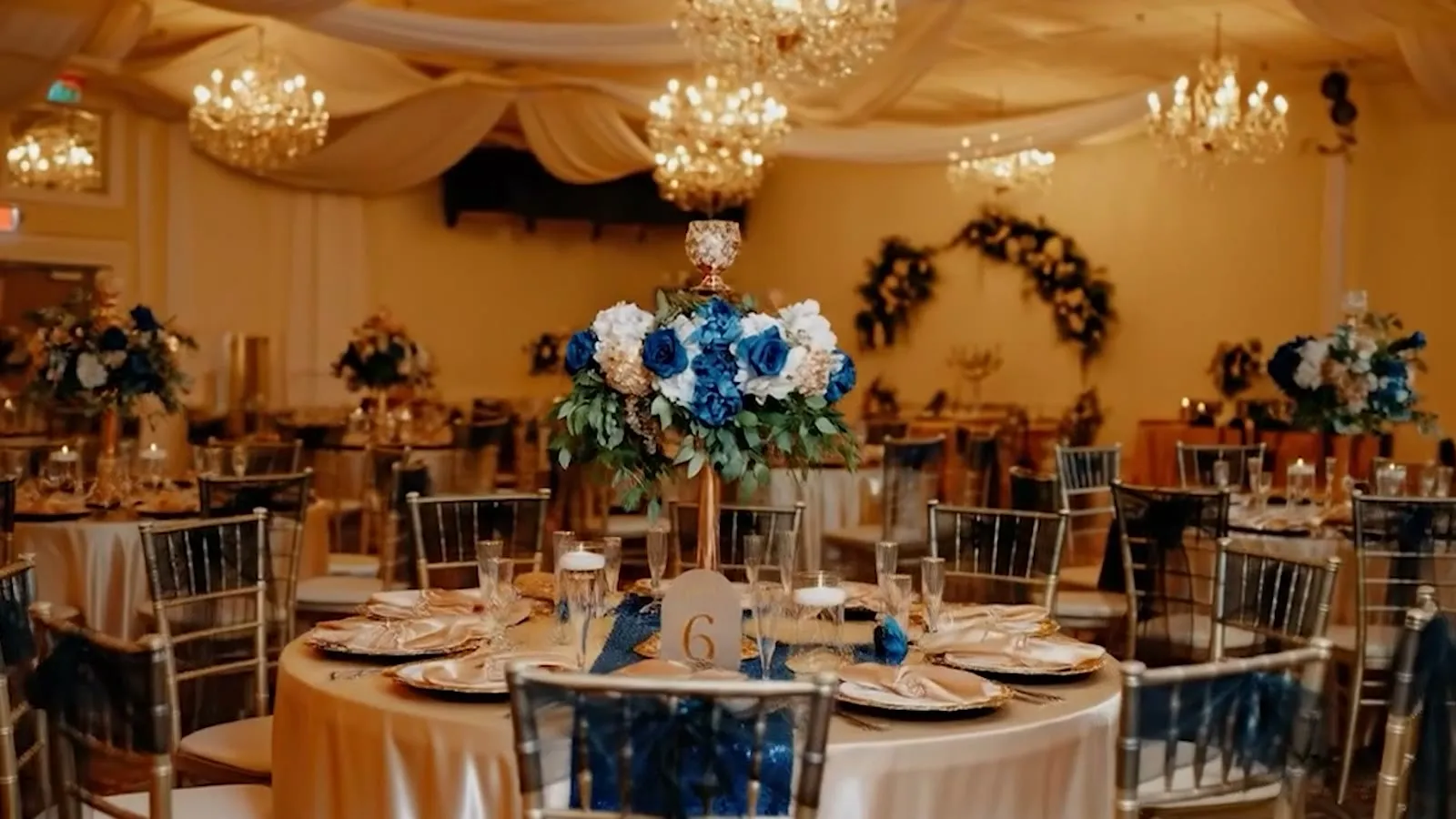 Diseño cálido del salón de Nencini Ballroom con mesas vestidas, sillas doradas, flores e iluminación nocturna