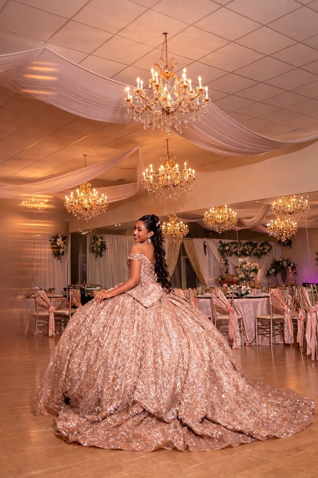 Retrato de quinceañera con vestido dorado bajo los candelabros y drapeados de Nencini Ballroom