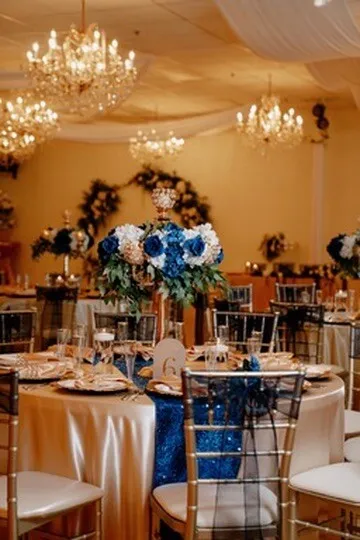 Montaje de recepción azul y blanco con candelabros, mesas redondas y sillas doradas en Nencini Ballroom