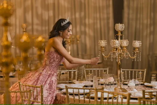 Quinceañera con vestido rosa ajustando un candelabro junto a decoración dorada en Nencini Ballroom