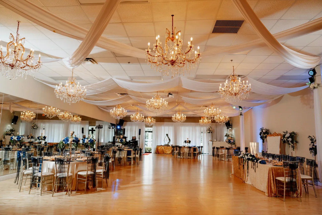 The ballroom at Nencini with chandeliers, a dance floor and navy-and-gold table settings