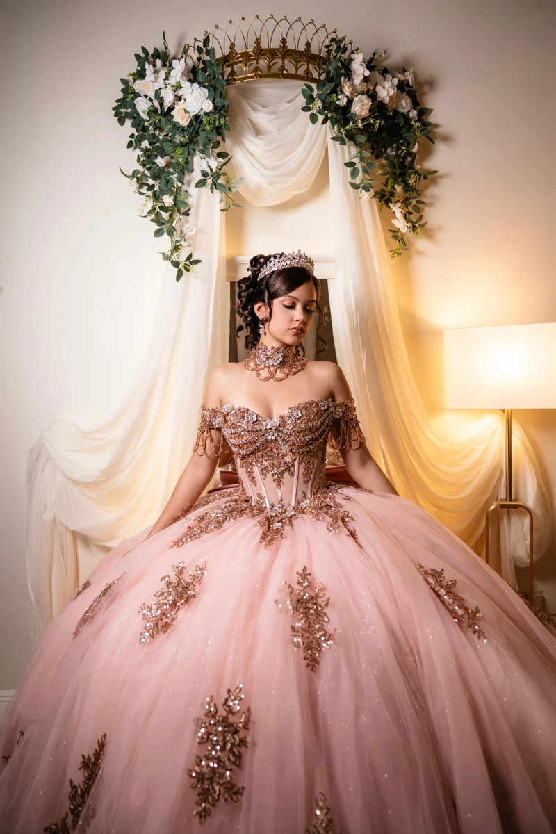 A quinceañera in a blush gown beneath a floral arch at Nencini Ballroom