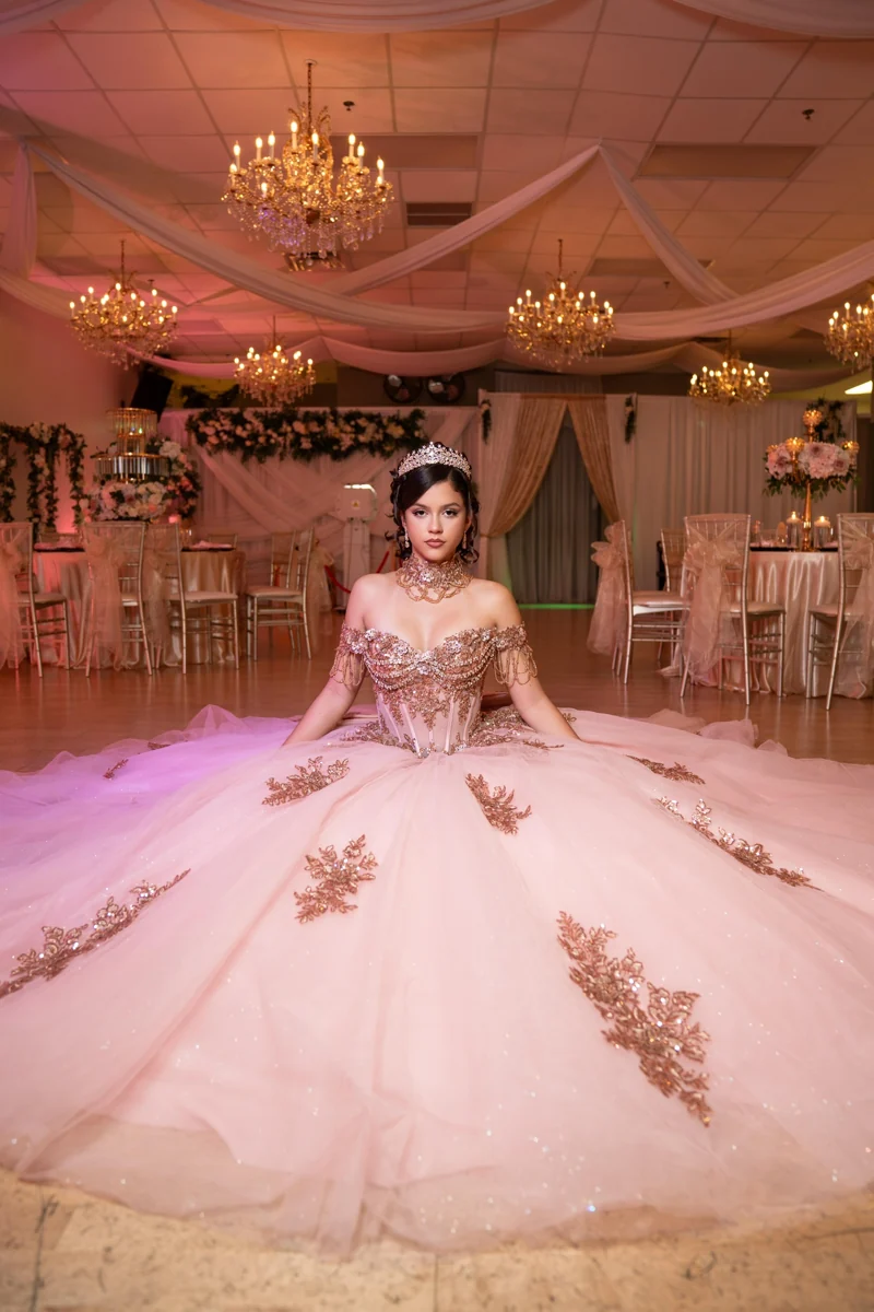 Quinceañera in a pale pink gown on the ballroom floor under chandeliers